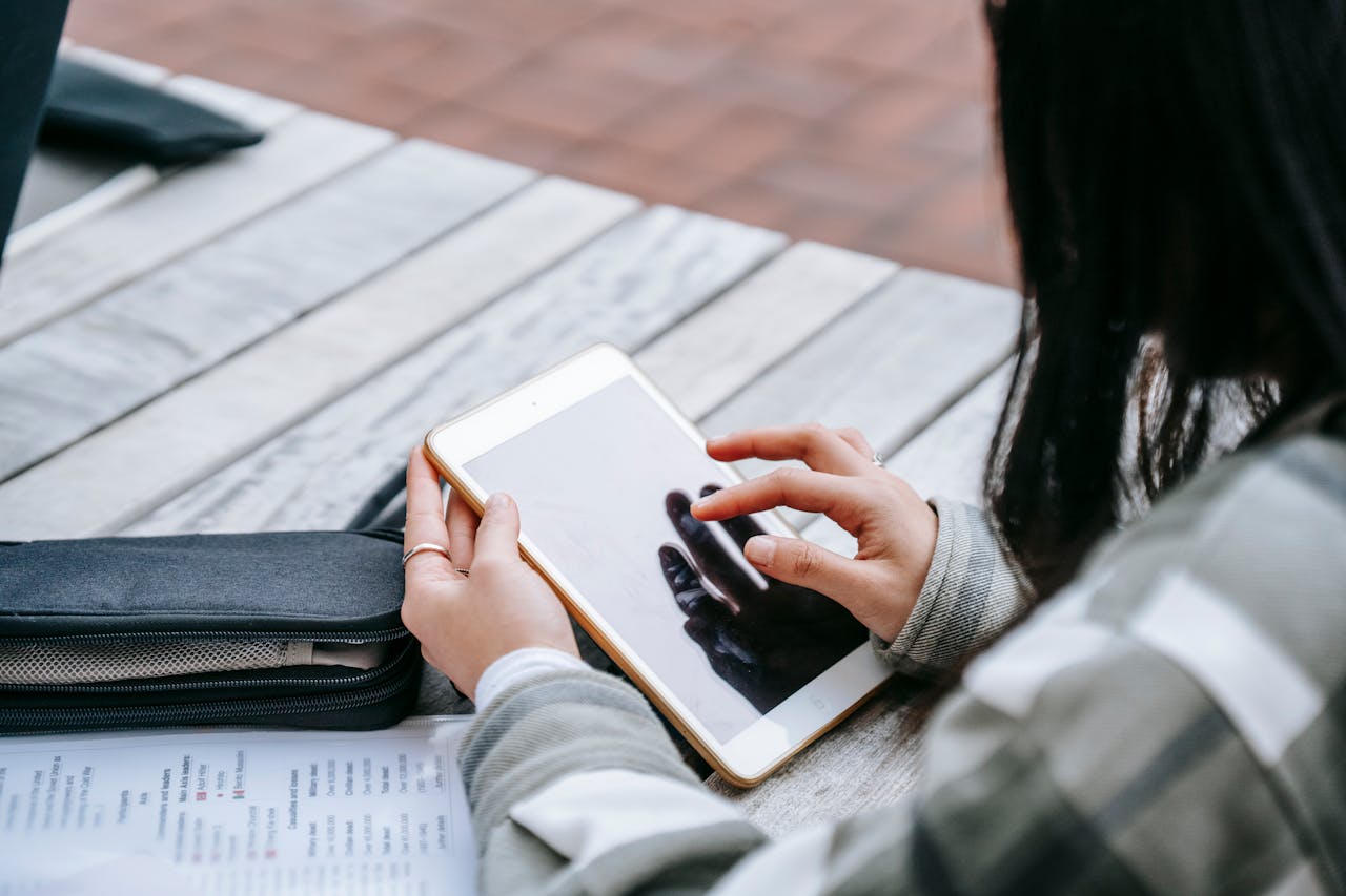 A young woman using a tablet for studying outdoors at a wooden table.